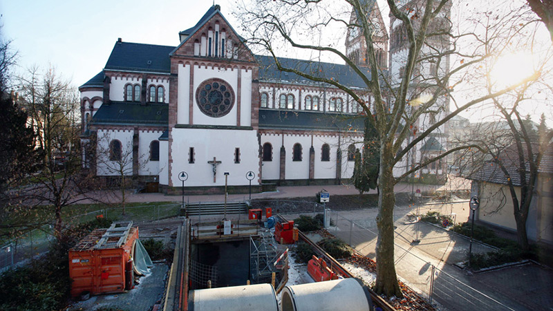 Bild der Baustelle in Offenburg und im Hintergrund ist die Kirche zu sehen mit Bäumen im Sonnenschein